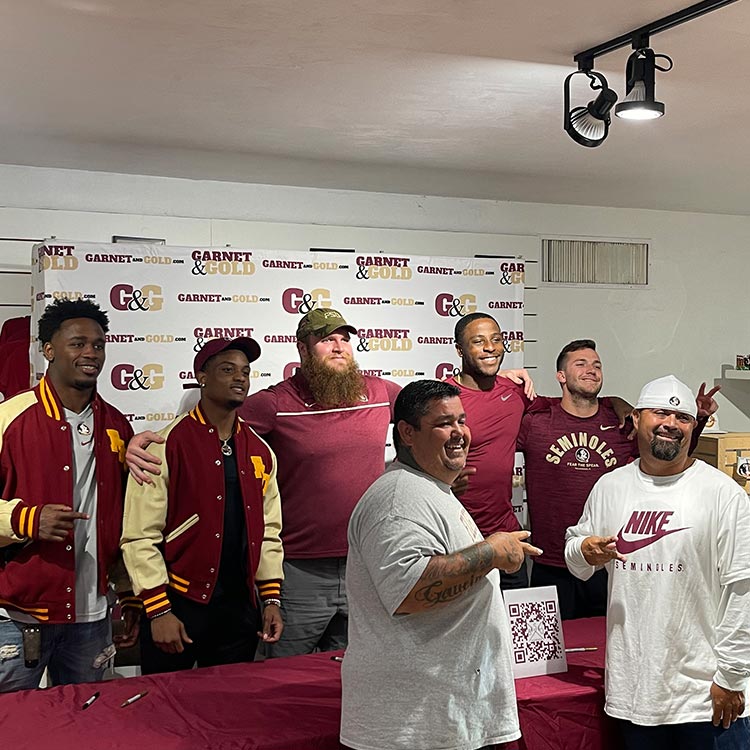 Dillan Gibbons posing with other football players in front of a Garnet & Gold banner