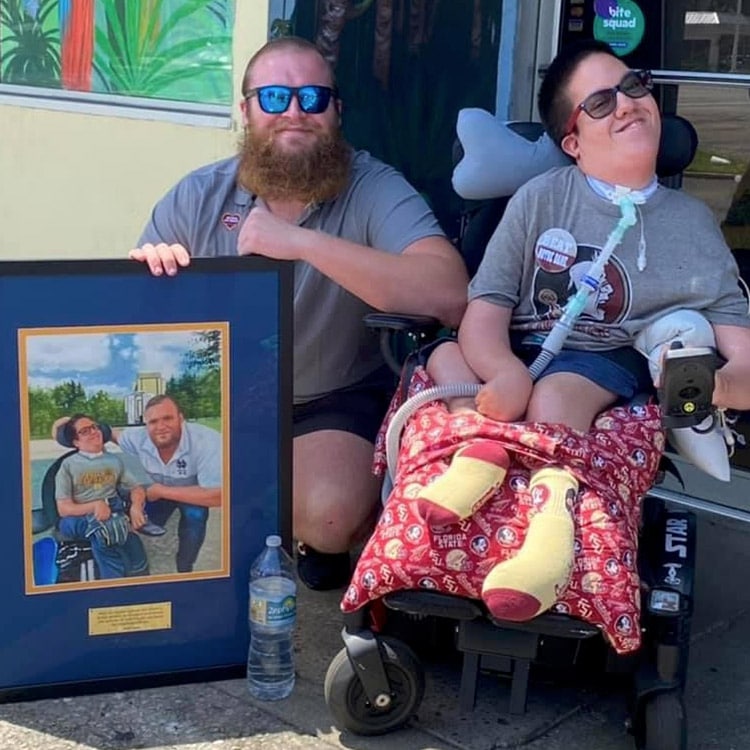 Dillan Gibbons posing with Timothy Donovan while holding a large, framed photo of the two of them