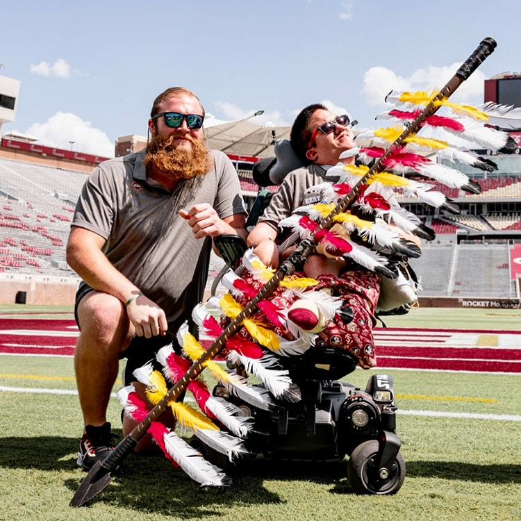 Dillan Gibbons posing with Timothy Donovan on the football field holding the FSU spear